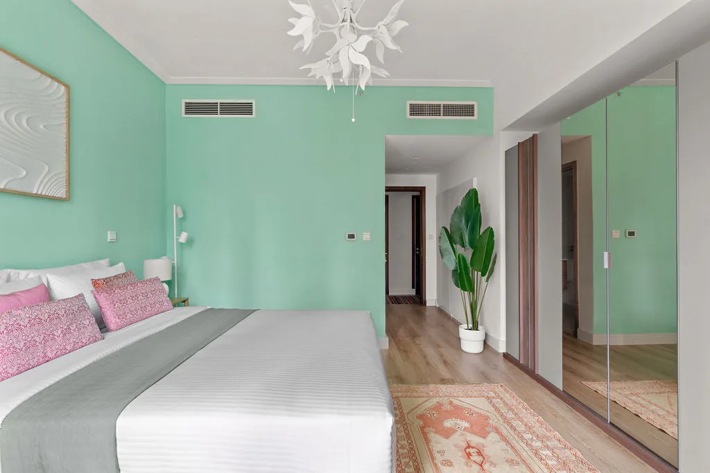 A bedroom with a bed, mirrored wardrobe, and potted plant beside the doorway.