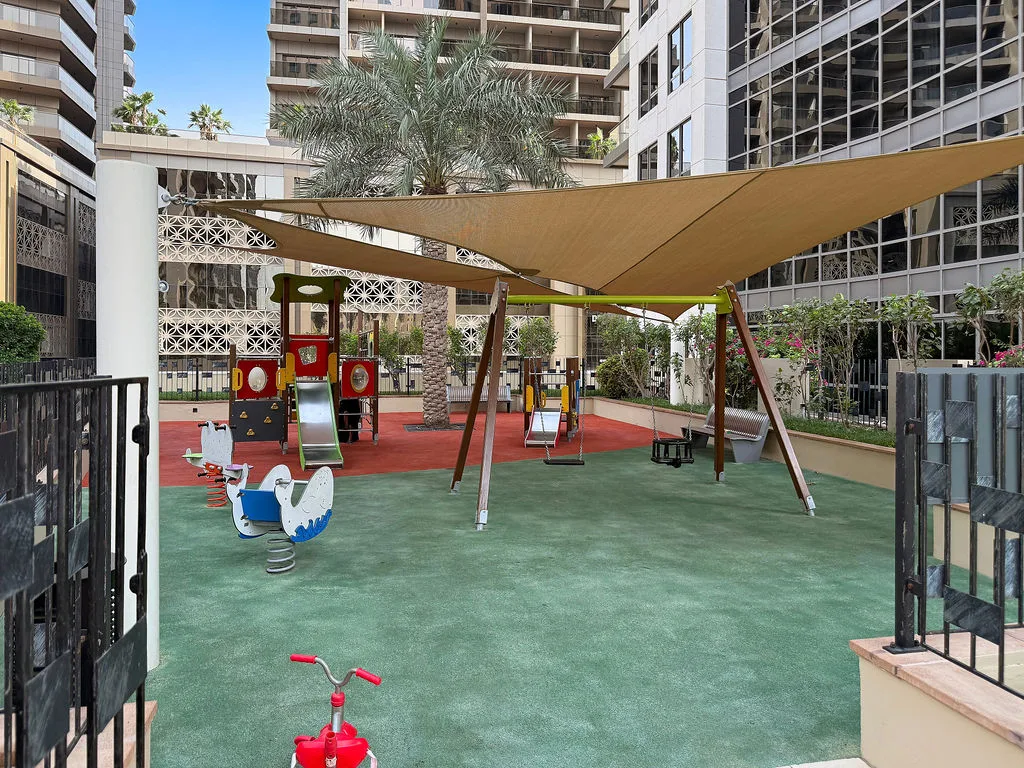 An outdoor playground with colorful play equipment beneath large shade sails.