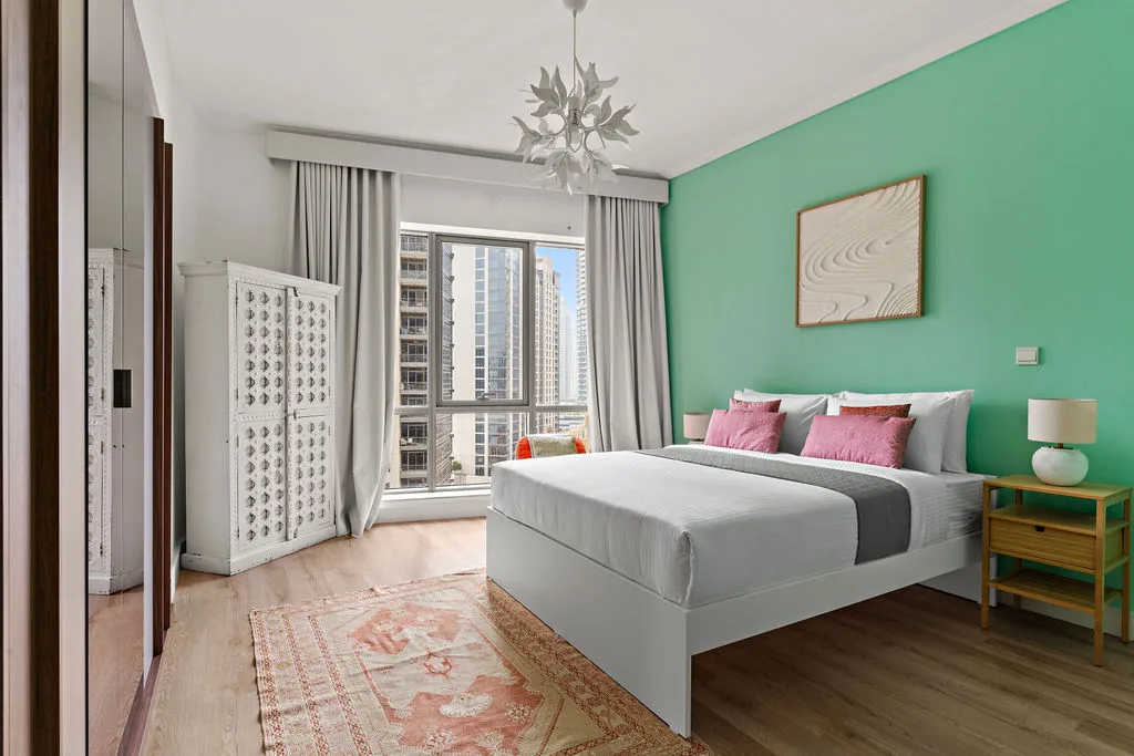 A bedroom with a bed, green accent wall, and large windows.