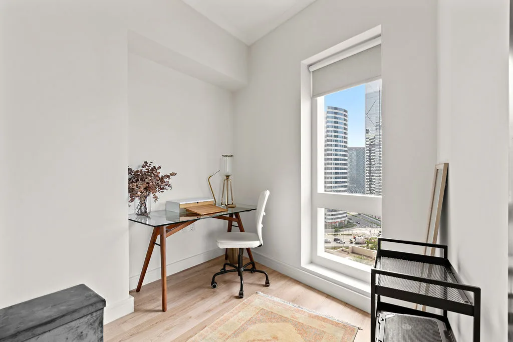 A bright workspace with a desk and chair beside a large window overlooking city buildings.