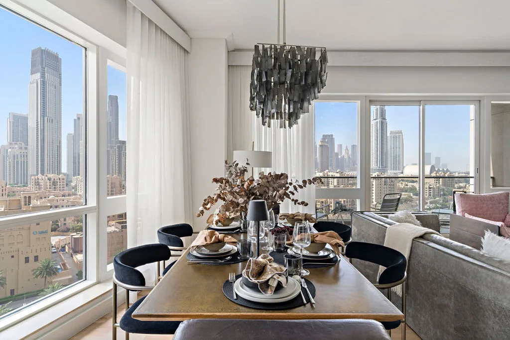 A dining area with a set table beside large windows overlooking the city.
