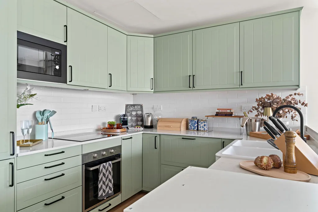 A modern kitchen with pale green cabinets, white counters, and a built-in oven.