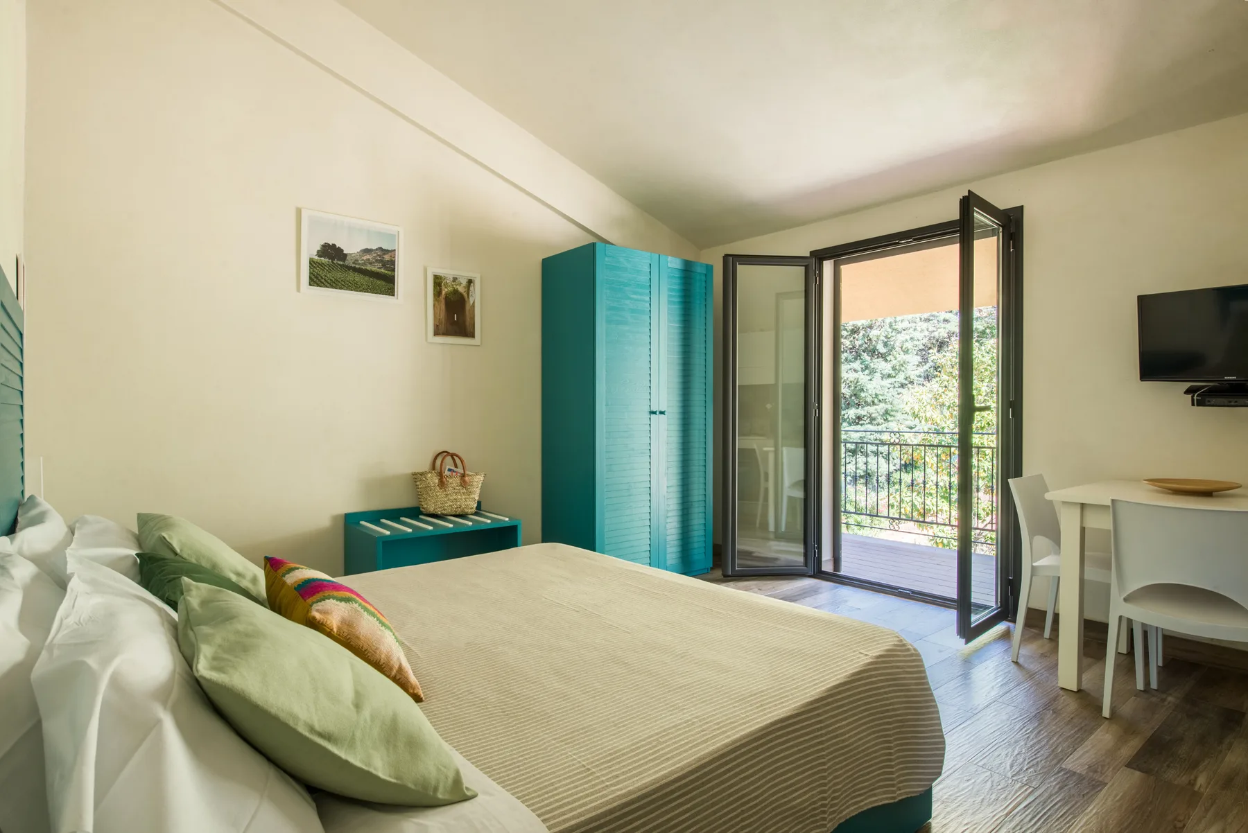 Un dormitorio con una cama, armarios turquesa y una puerta abierta al balcón.