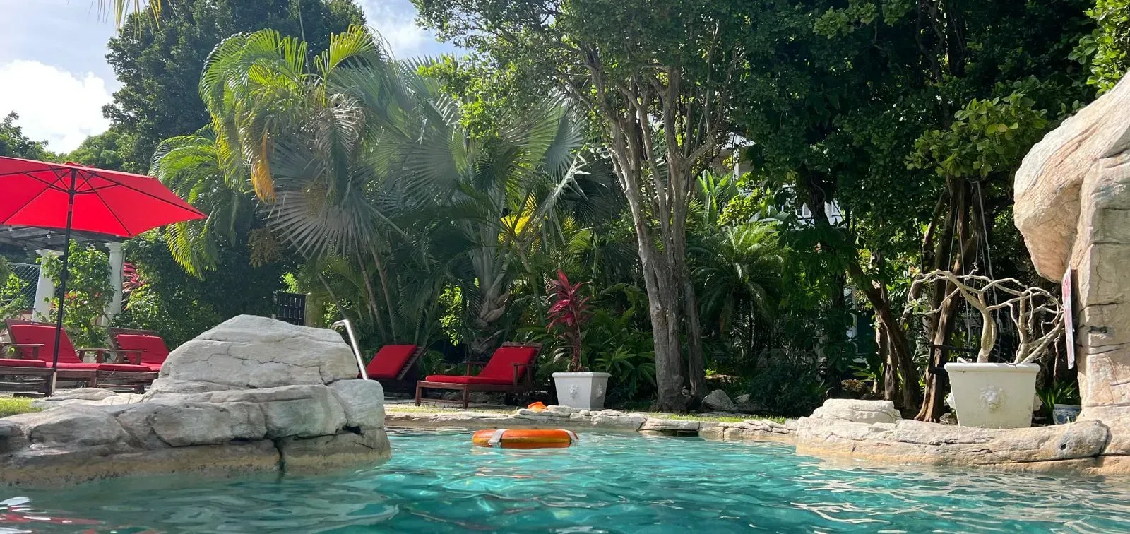 Piscina rodeada de rocas, vegetación y sombrillas rojas