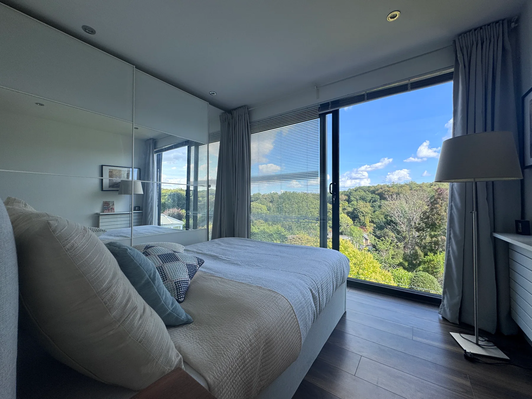 A bedroom with a bed beside large windows overlooking green hills.
