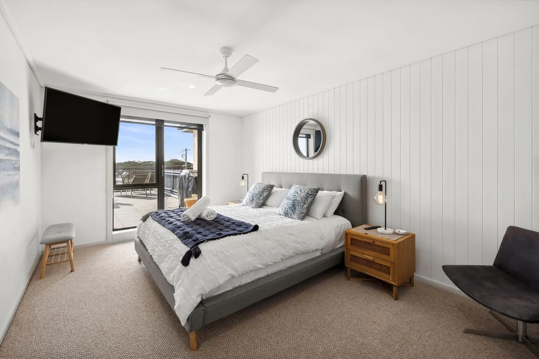 A bright bedroom with a bed beside sliding glass doors opening to a balcony.
