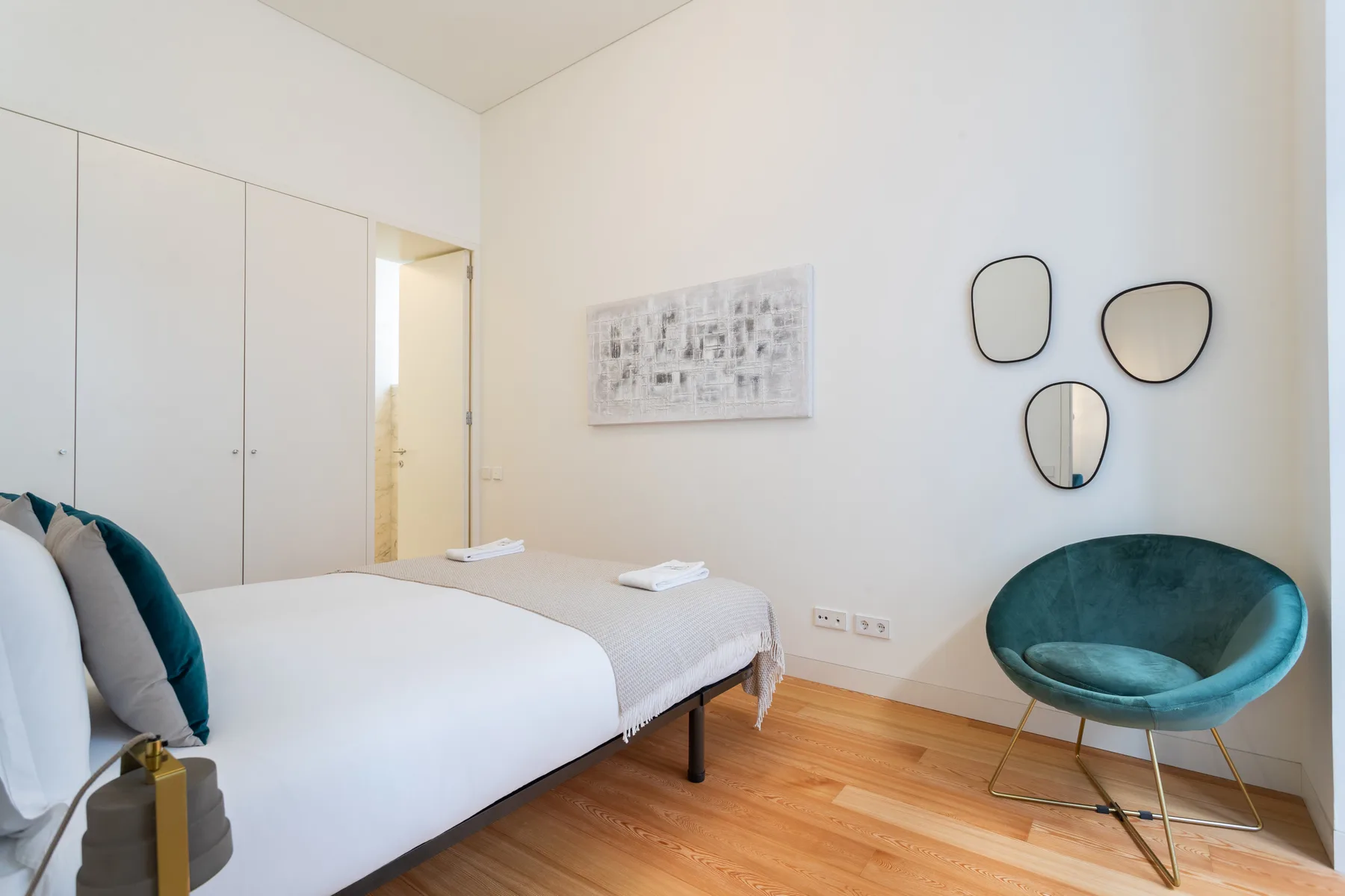 Un dormitorio luminoso con una cama y una silla verde azulado junto a la pared.