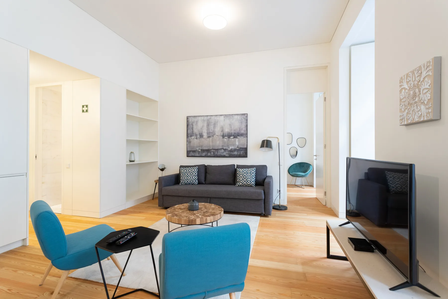 Una sala de estar luminosa con un sofá, asientos azules y un televisor.