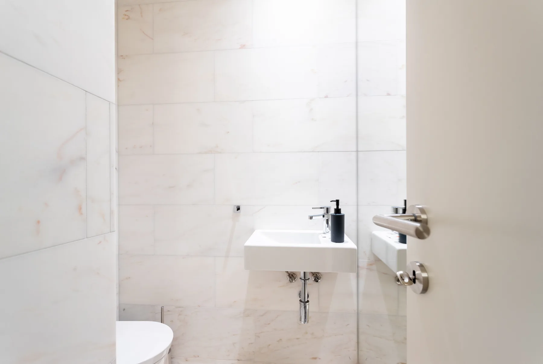 Un baño luminoso con un lavabo suspendido y paredes de azulejos claros.