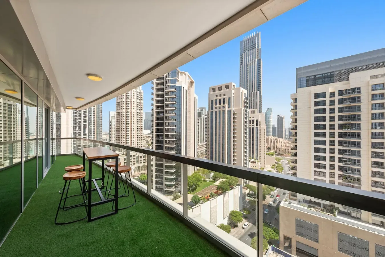 A balcony with green flooring and a small table overlooks a city skyline.
