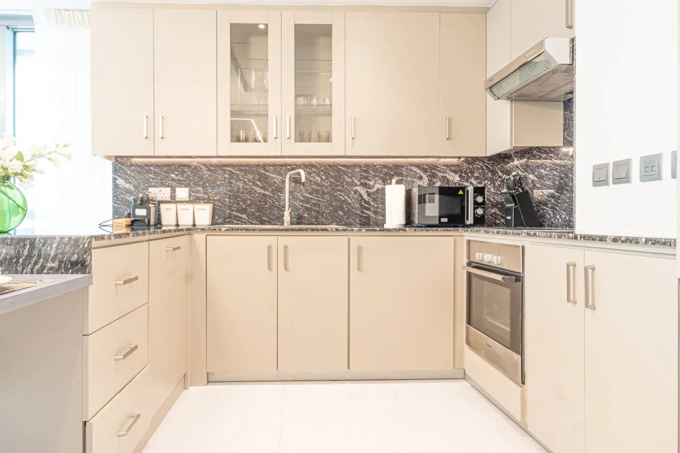 A bright kitchen with pale cabinets, dark countertops, and built-in appliances.