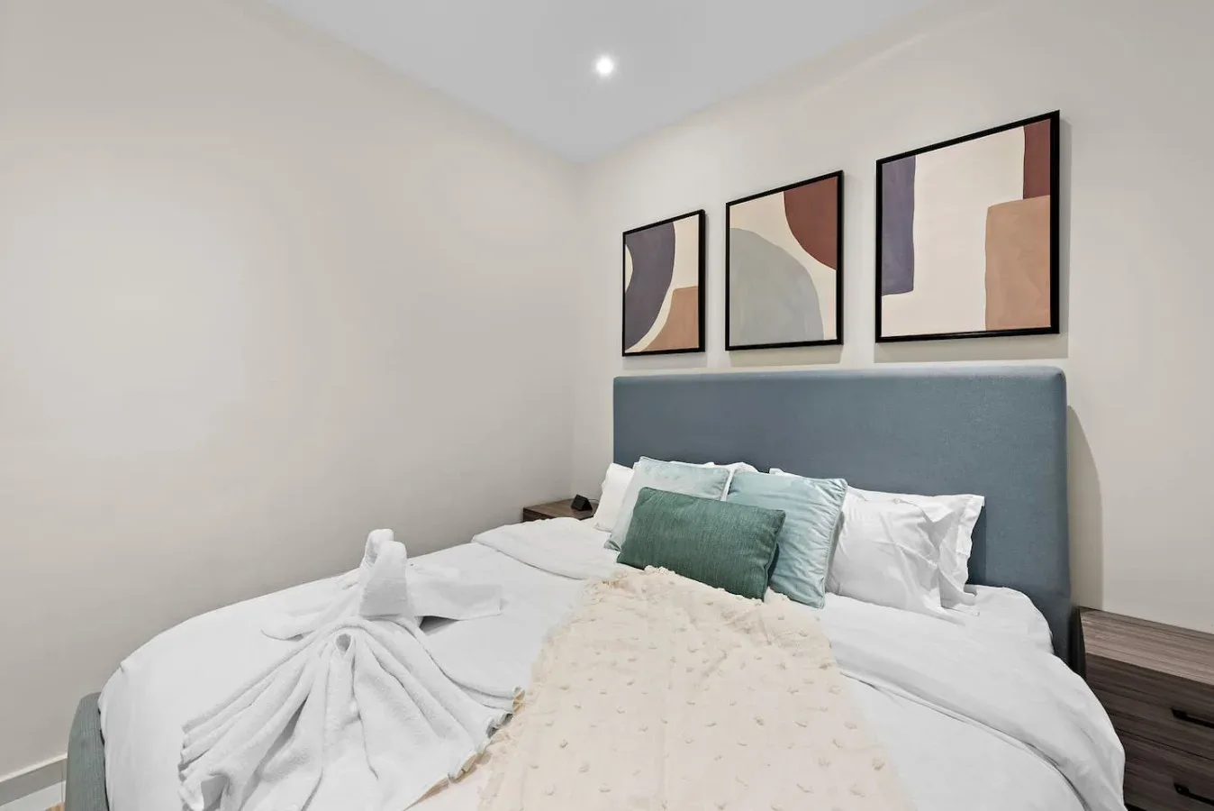 A bedroom with a neatly made bed beneath three framed abstract prints.