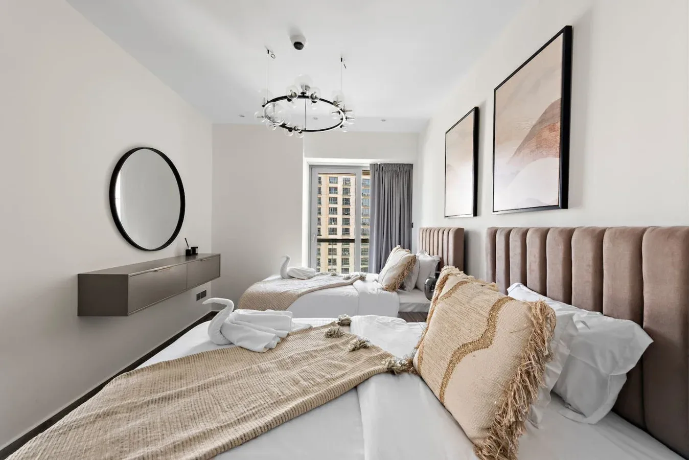 A bright bedroom with two beds, neutral bedding, and framed artwork.