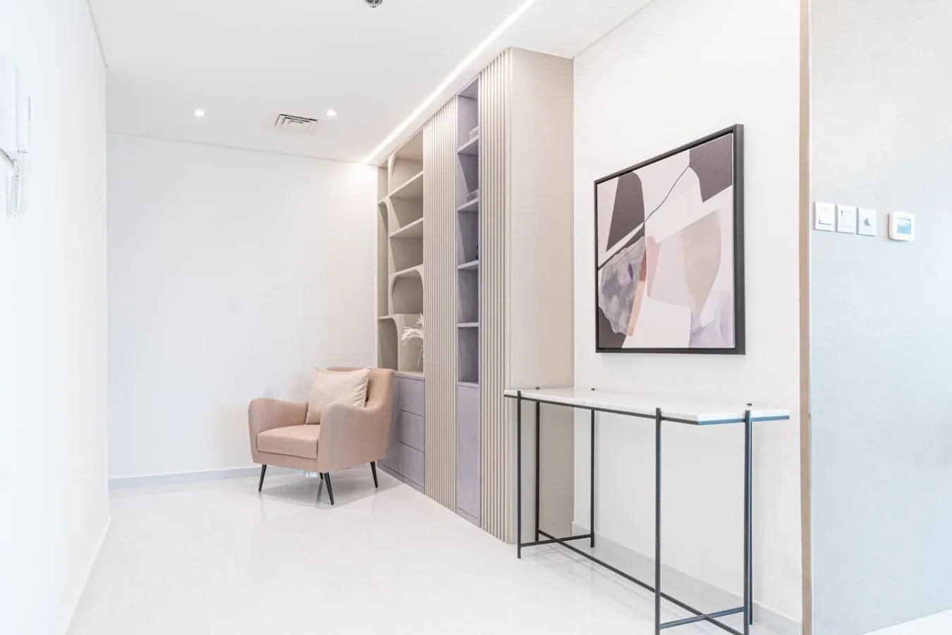 A bright interior hallway with built-in shelving, a small seating area, and framed artwork.