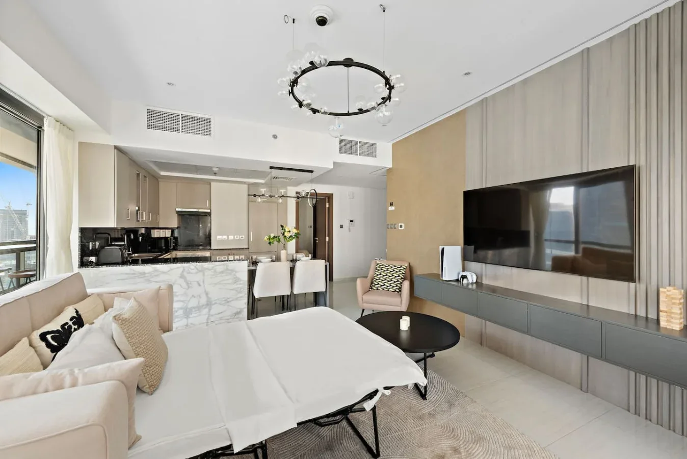 A modern living room with a sofa, dining table, and large wall-mounted television.