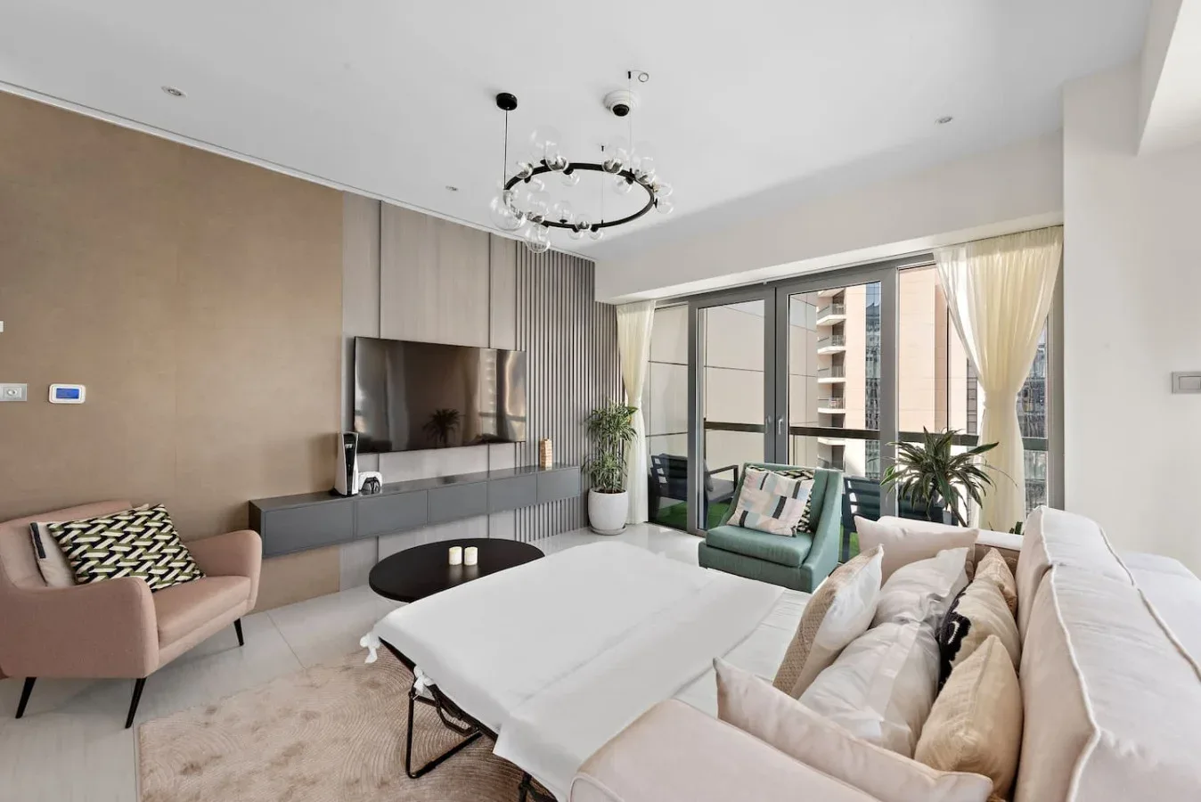 A bright living room with seating, a wall-mounted television, and large windows.