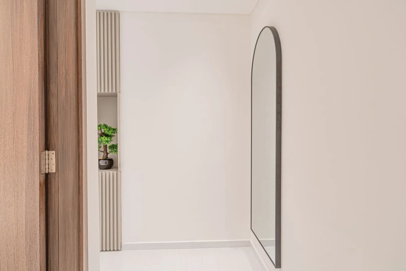 A bright hallway features a tall arched mirror and a small potted plant.