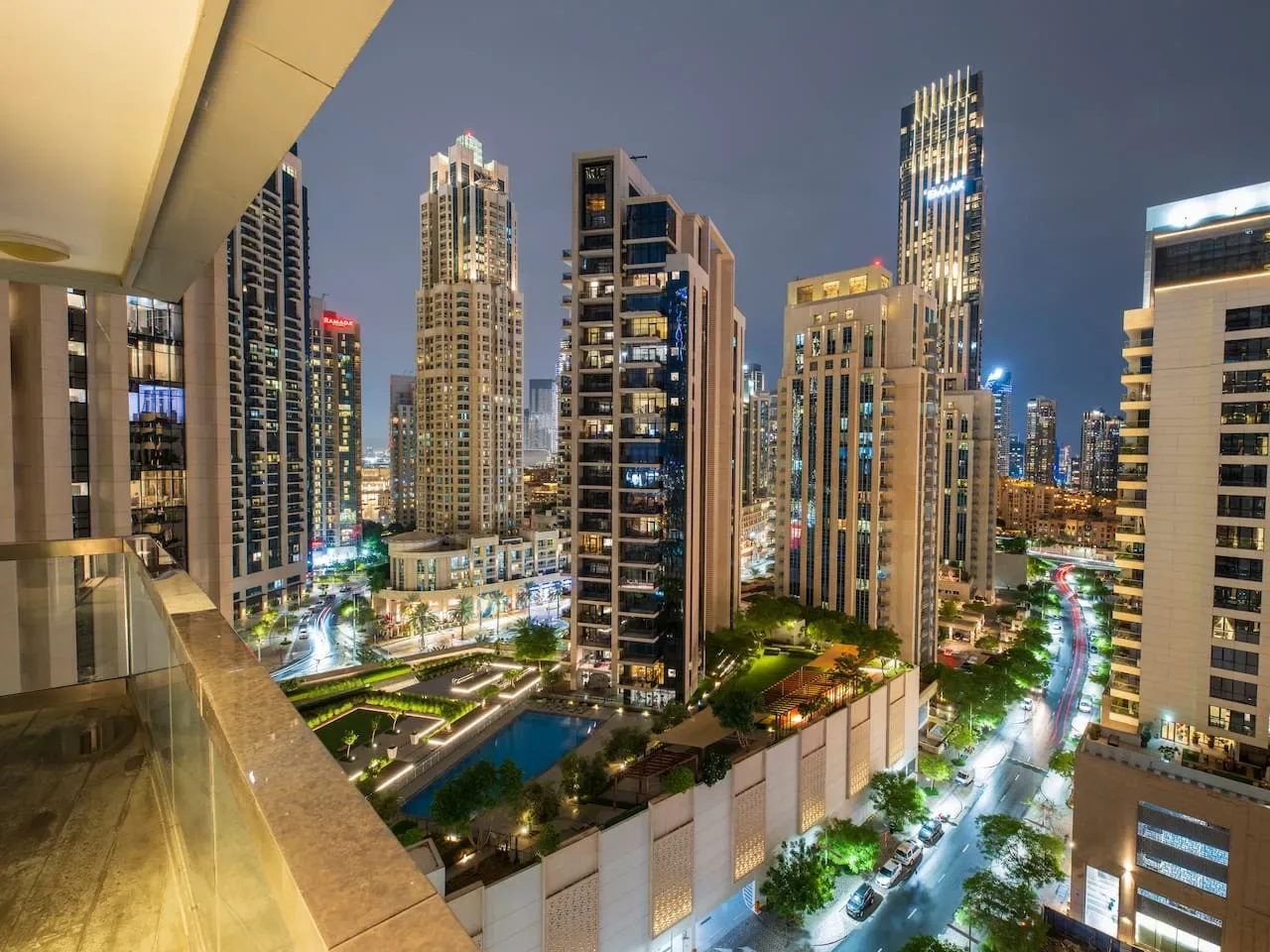 A nighttime cityscape of illuminated high-rise buildings viewed from a balcony.