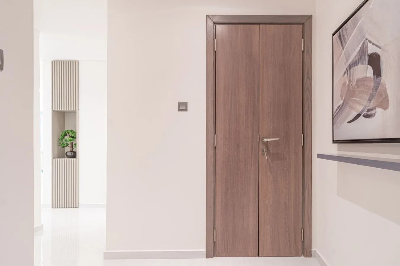 A bright interior hallway with a wooden door and framed artwork.