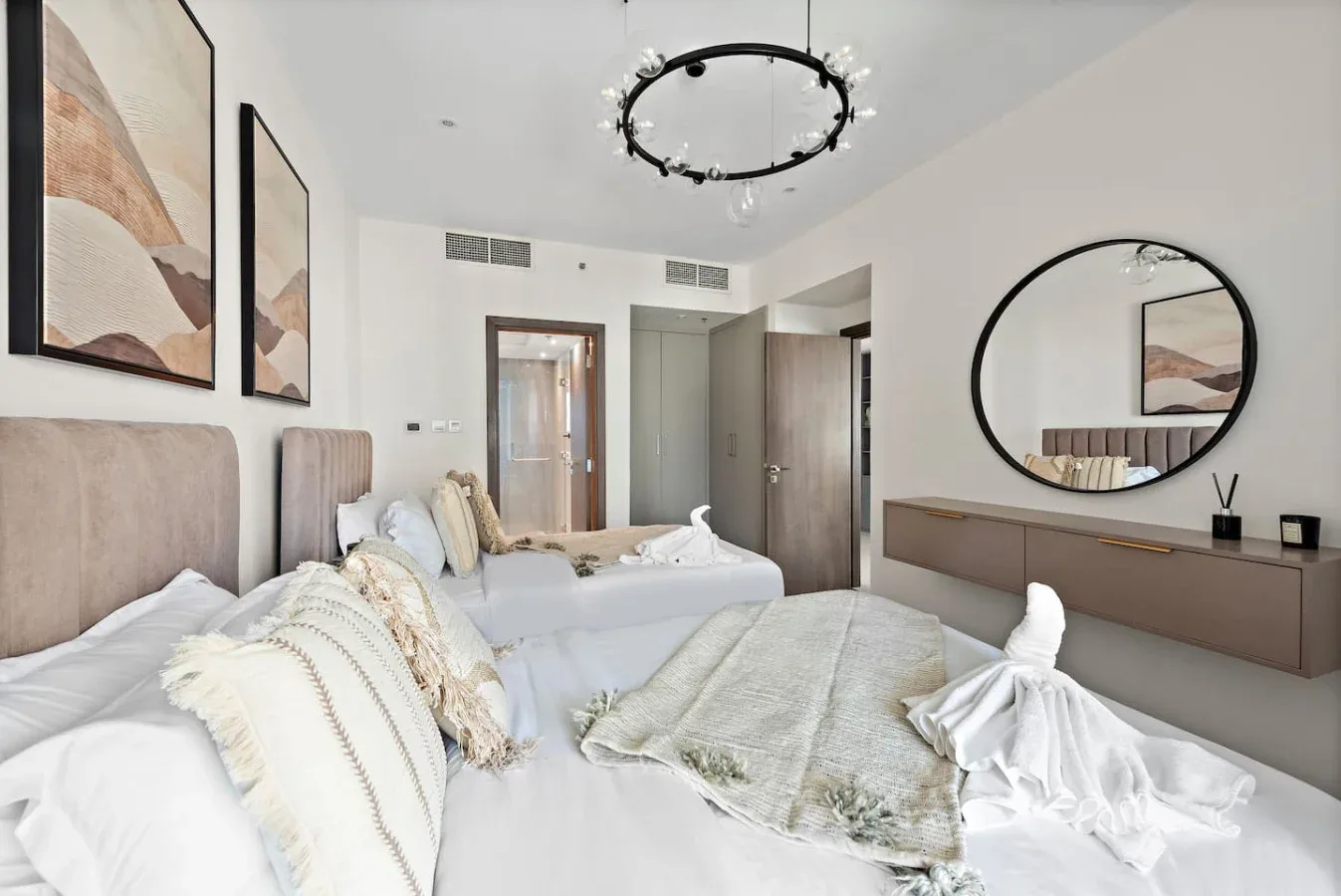 A bedroom with two beds, neutral bedding, and framed abstract artwork.