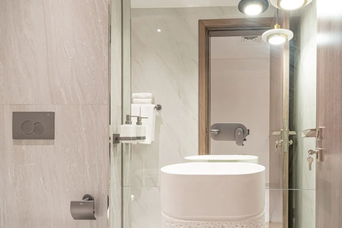 A bright bathroom with a large sink, glass shower enclosure, and wall-mounted fixtures.