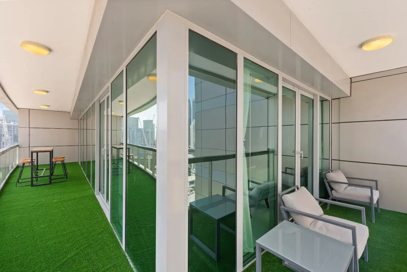 A glass-walled patio with green turf and outdoor seating.