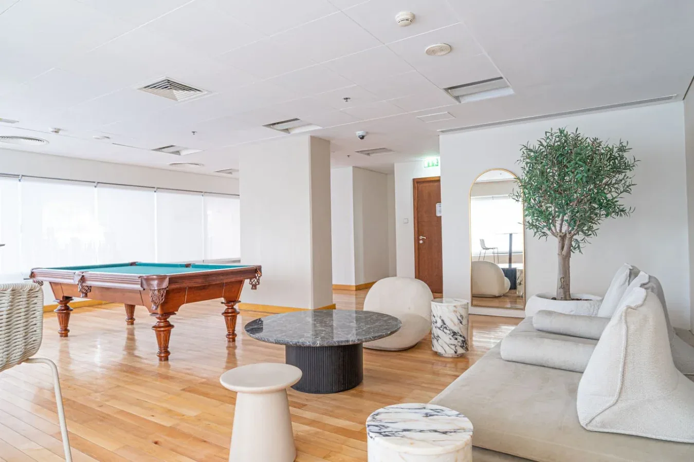 A lounge with a billiards table, low seating, and a potted tree.