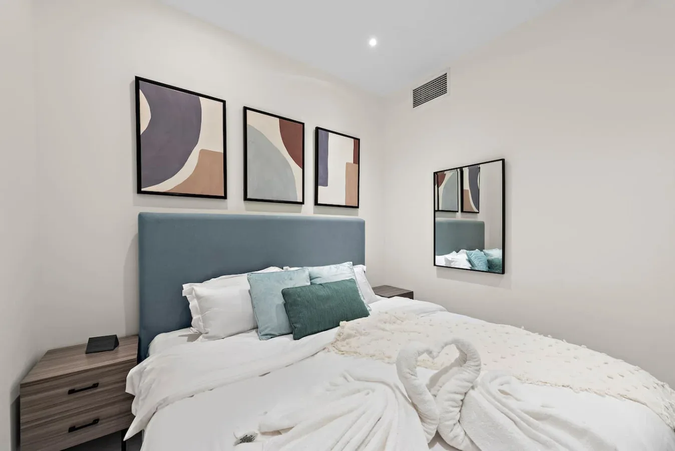 A bedroom with a neatly made bed and abstract artwork above the headboard.