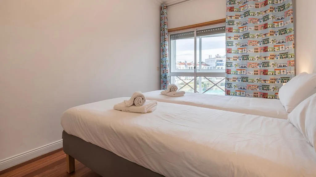Un dormitorio con una cama bien tendida junto a una ventana grande.