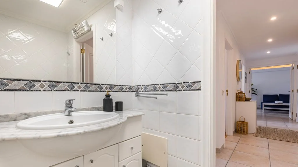 Un baño luminoso con azulejos, lavabo y vista a la habitación contigua.