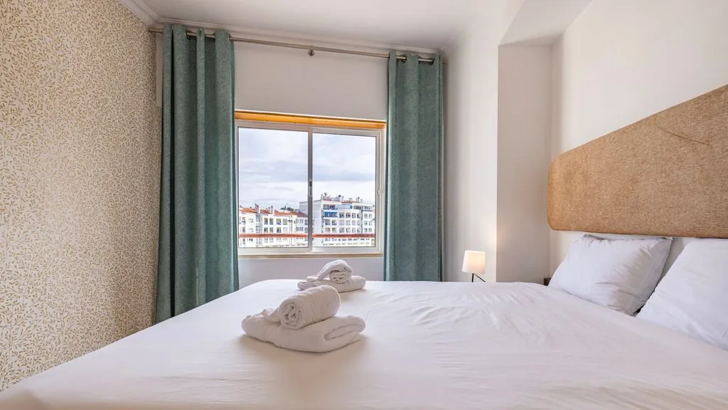 Un dormitorio con una cama bien arreglada y cortinas verde azulado junto a la ventana.