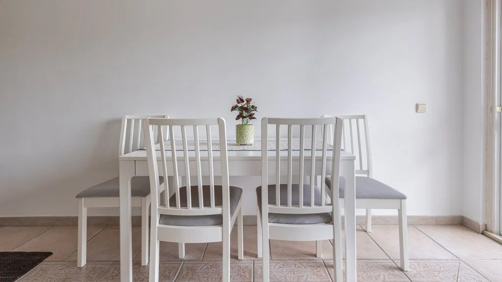 Un comedor con una mesa blanca y sillas junto a una pared lisa.