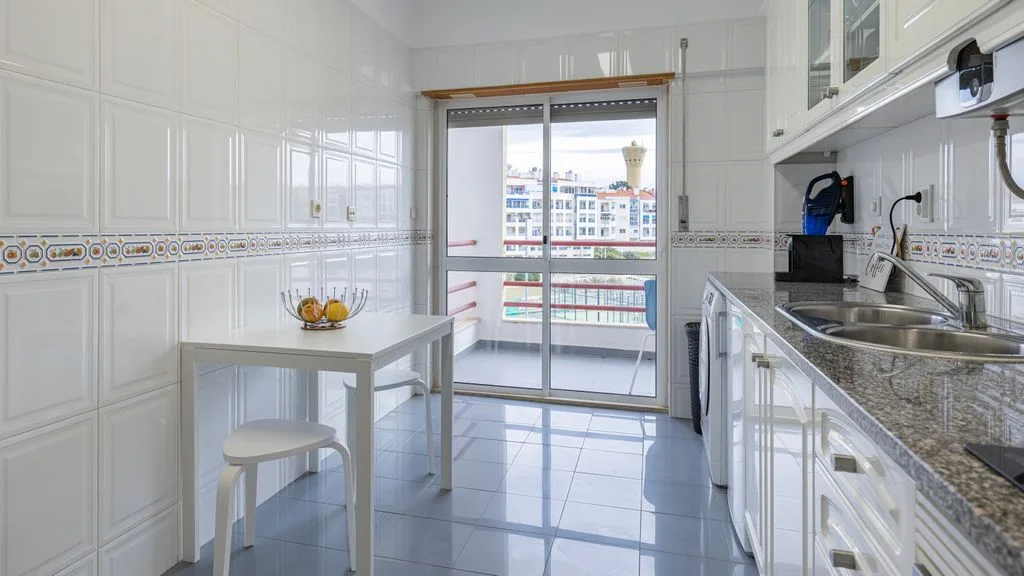 Una cocina luminosa con armarios blancos y una mesa pequeña.