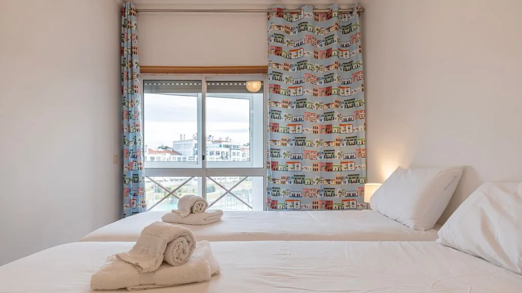 Un dormitorio con una cama bien hecha y cortinas estampadas junto a la ventana.