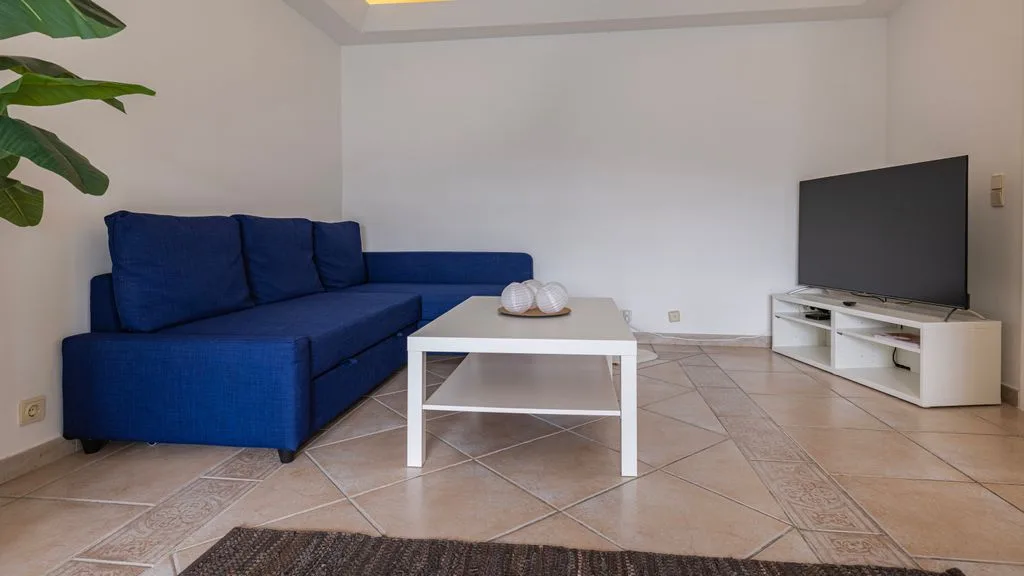 Una sala de estar con asientos azules, una mesa de centro y un televisor.