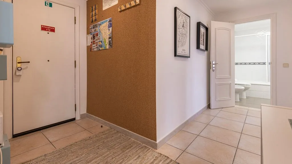 Pasillo de un apartamento con una puerta de entrada, cuadros y una puerta abierta al baño.