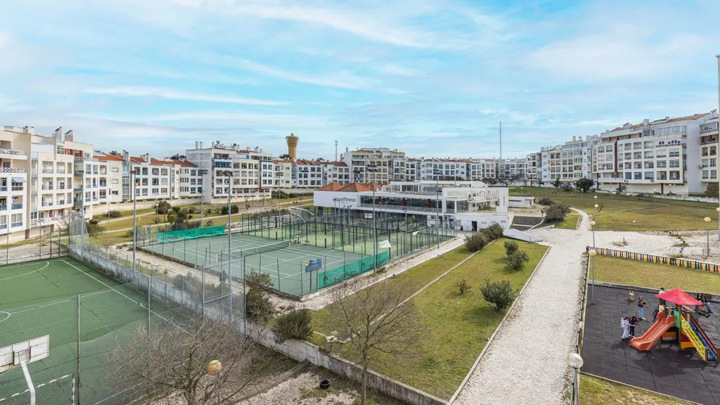 Complejo residencial con canchas deportivas cercadas, senderos ajardinados y un área de juegos.