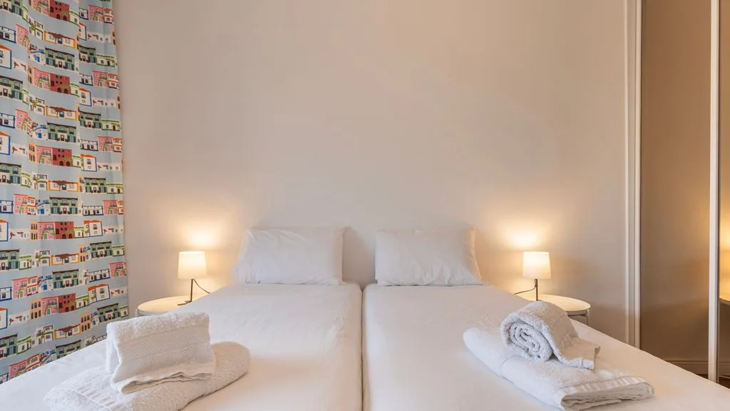 Un dormitorio con dos camas, lámparas de noche y toallas dobladas.
