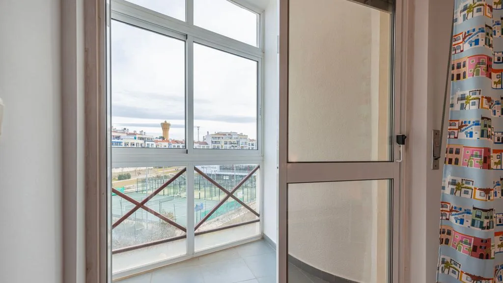 Una habitación luminosa con grandes ventanas que dan a edificios cercanos y una barandilla.