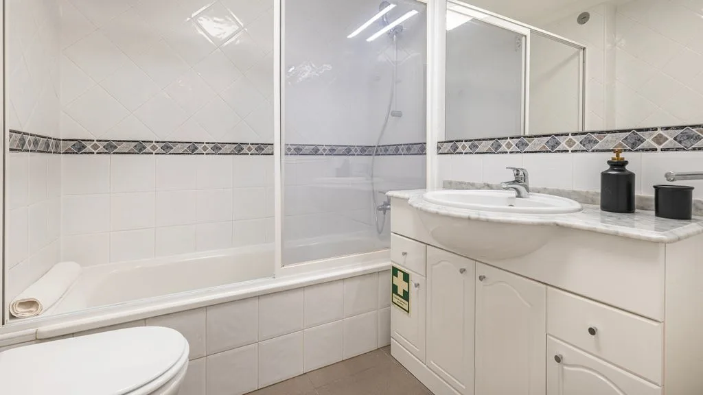Un baño luminoso con bañera, mampara de ducha de cristal y lavabo.