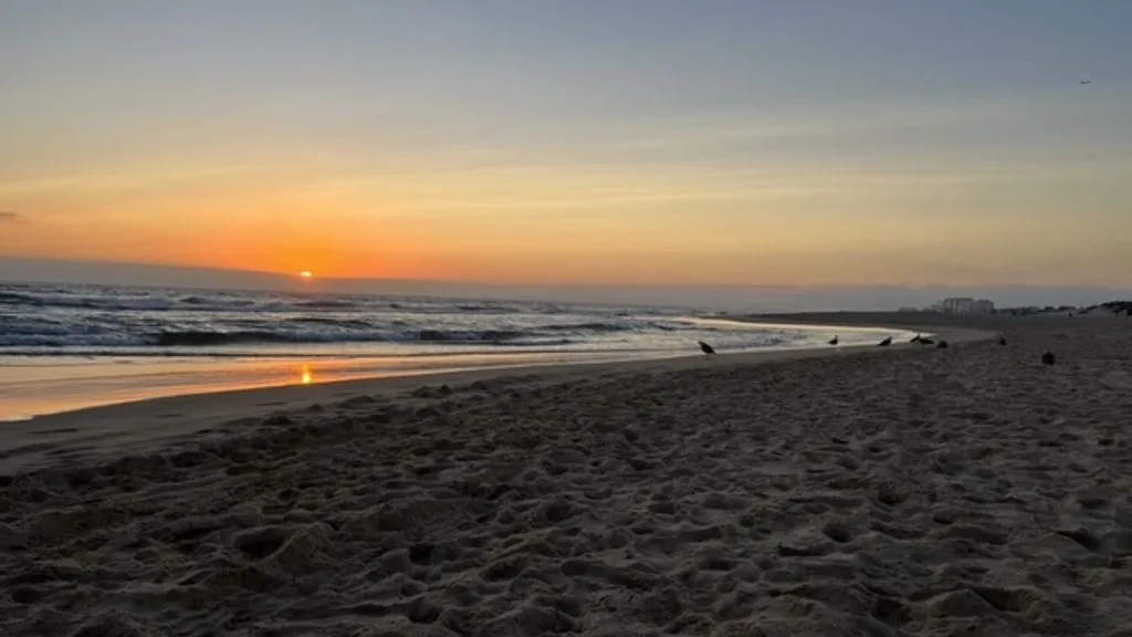 Una playa al atardecer, con olas suaves llegando a la orilla.