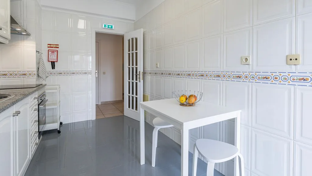 Una cocina alicatada con armarios blancos y una pequeña mesa de comedor.