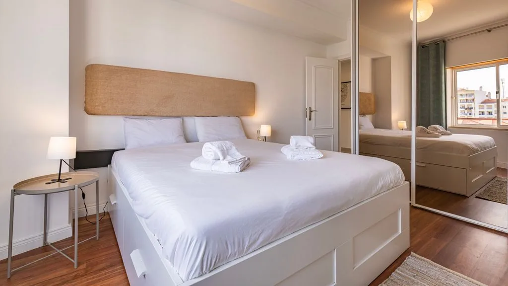 Un dormitorio luminoso con una cama tendida y puertas de armario con espejo.