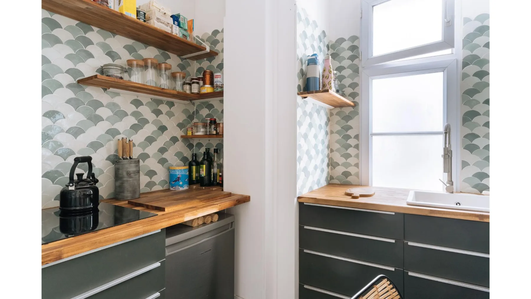 Una cocina con gabinetes oscuros, encimeras de madera y azulejos estampados.