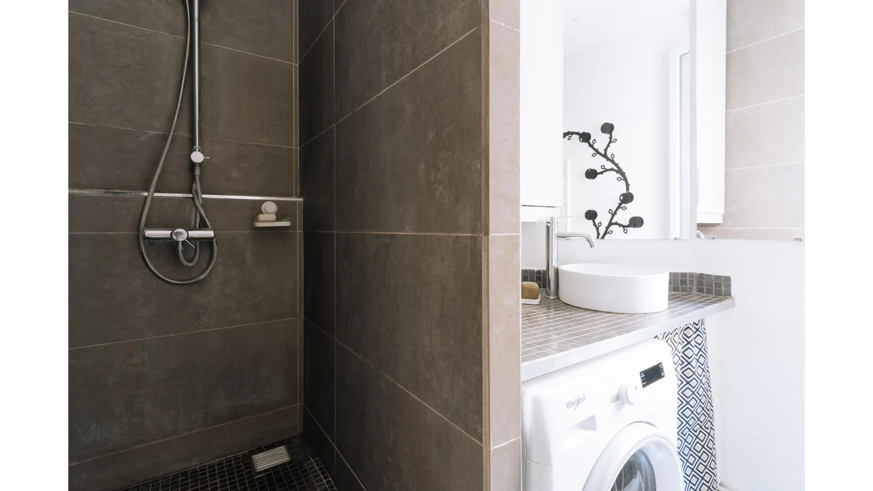 Un baño con azulejos, ducha de pared y lavabo sobre una lavadora.