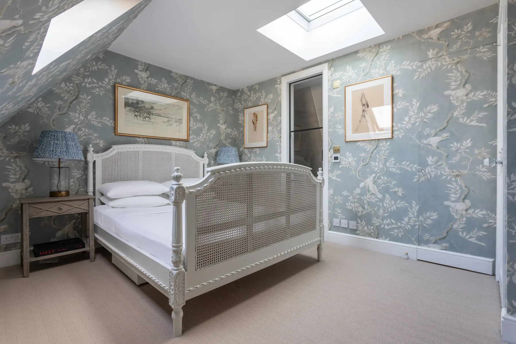 Un dormitorio con una cama blanca, papel tapiz floral y una claraboya.
