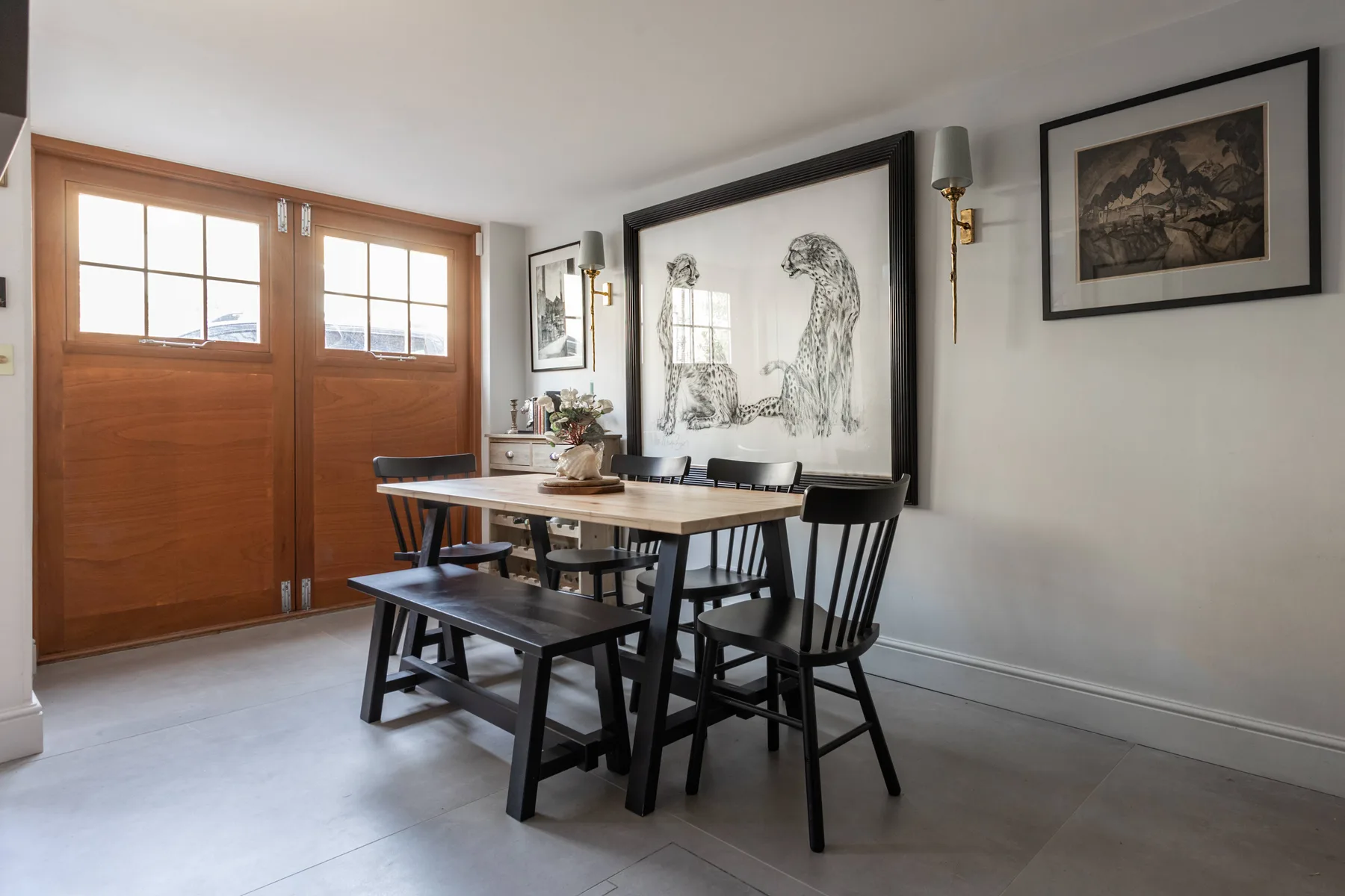 Comedor con una mesa de madera, asientos oscuros y obras enmarcadas.
