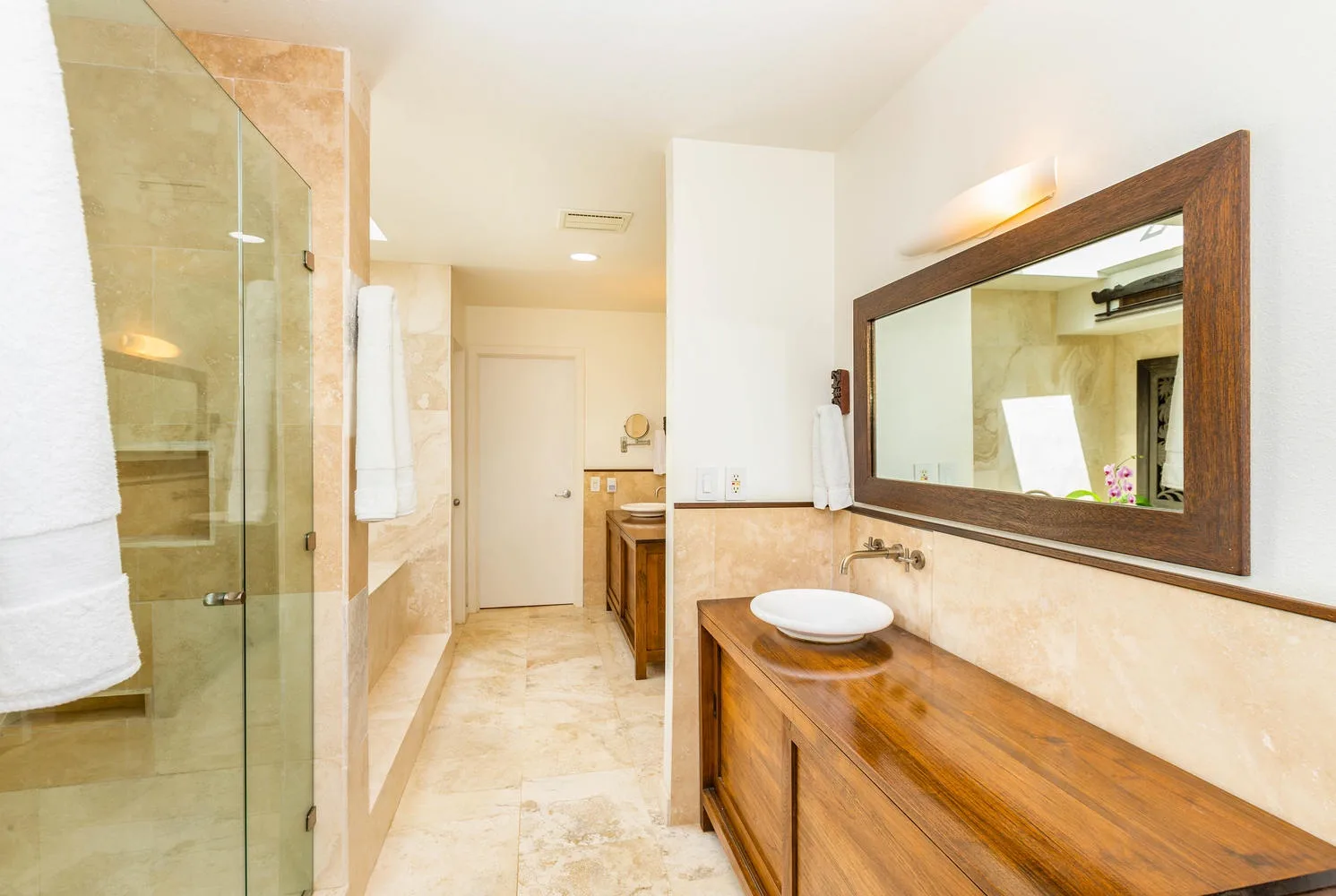 A bright bathroom with a glass shower and a wooden vanity beneath a large mirror.