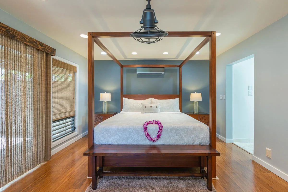 A bedroom with a canopy bed, bedside lamps, and woven window blinds.