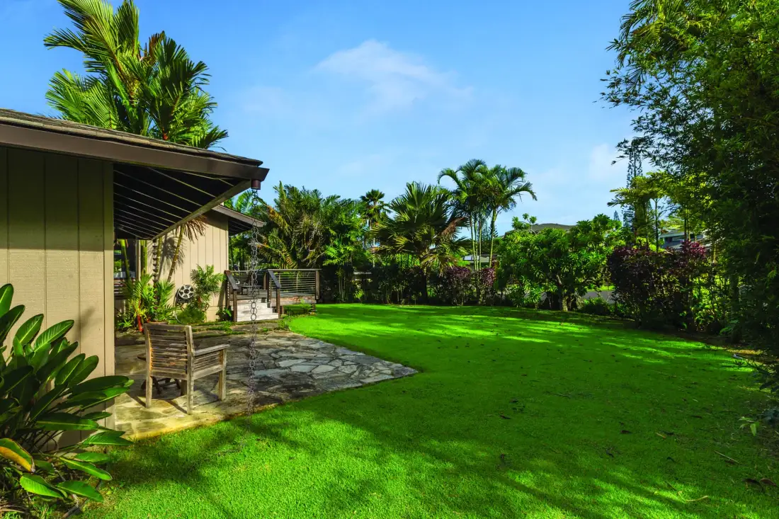 A landscaped garden with a broad green lawn and a paved patio beside a building.
